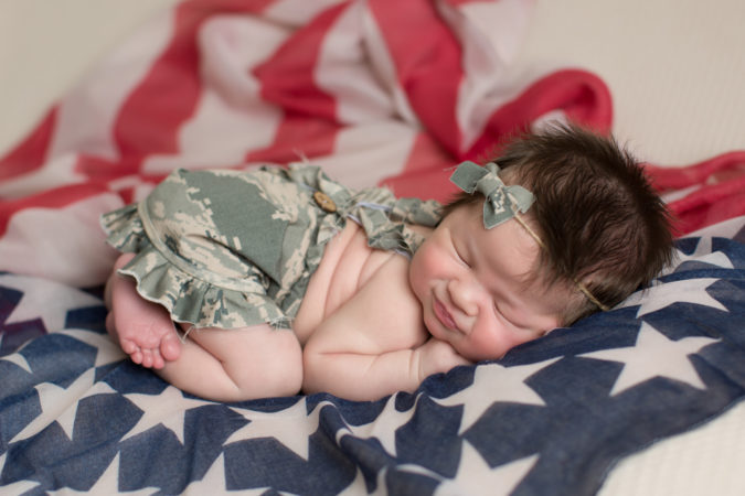 Newborn girl laying on American flag wearing Air Force outfit at Sarah Botta Photography's Studio in Woodbridge, VA
