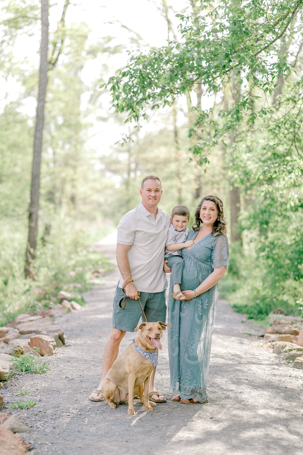 Maternity session outdoors with Sarah Botta Photography. Family image looking at camera with dog and young boy surrounded by trees.
